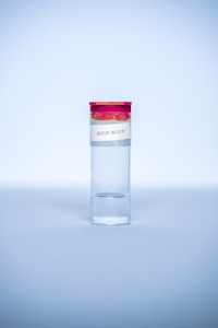 A clear test tube with a red cap and a label that reads '2019-NCOV' is placed upright against a light blue background. The tube is primarily filled with a clear liquid.