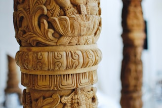 Artisan carefully carving intricate wooden designs on a teakwood pillar.