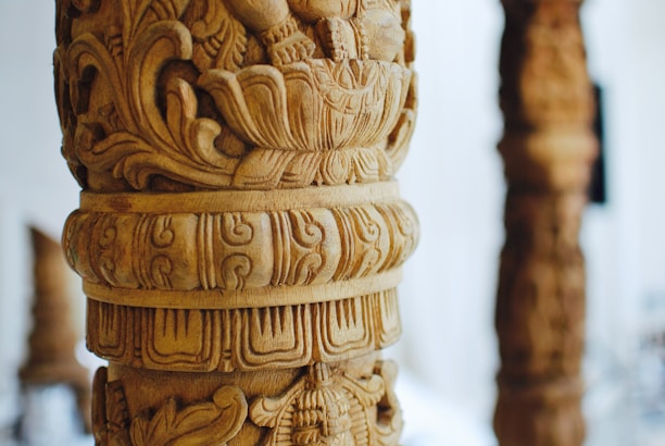Artisan carefully carving intricate wooden designs on a teakwood pillar.
