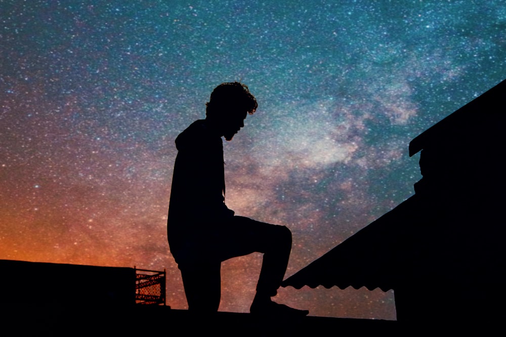 silhouette of man standing on roof under blue sky