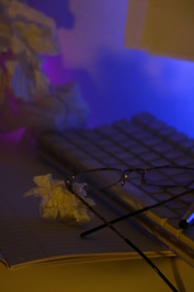 A cozy desk with a vintage eyeglasses case and a notebook beside a softly glowing lamp.