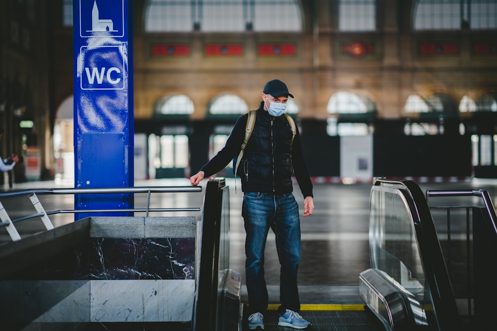 woman in black jacket and blue denim jeans standing on escalator