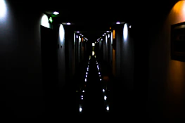 A dimly lit corridor drenched in deep reds and charcoals, with flickering static on old screens.