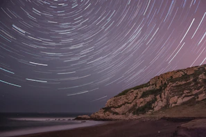 A time-lapse style shot showing star trails circling above a rocky outcrop