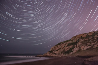 A time-lapse style shot showing star trails circling above a rocky outcrop