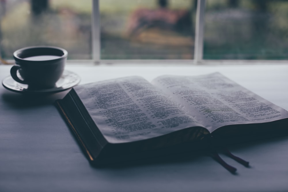 white book page beside black ceramic mug on table