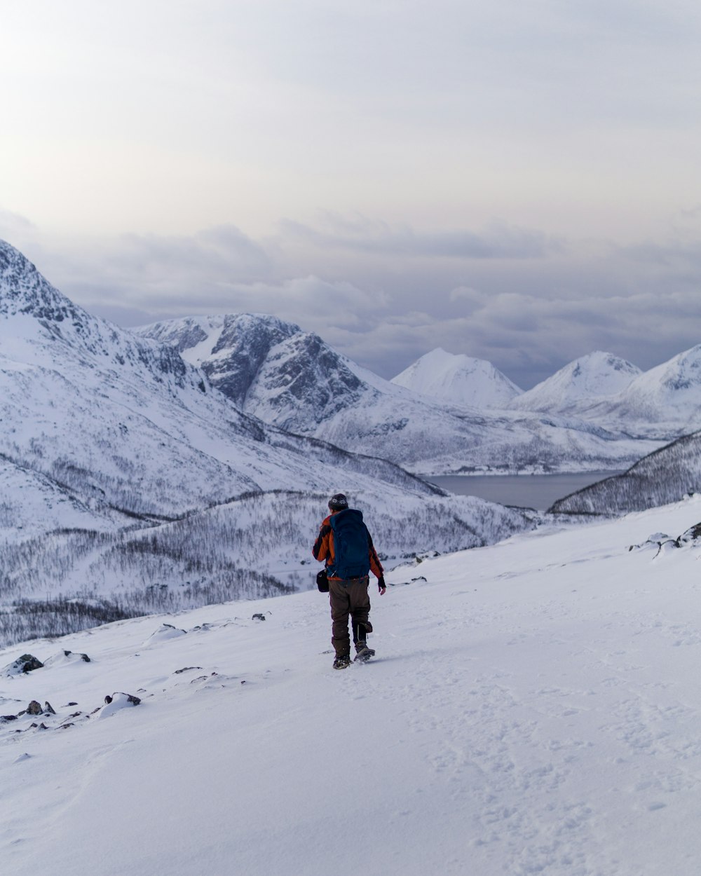 man in red jacket and black pants walking on snow covered ground during daytime