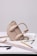 A stylish beige handbag with a unique sculptural design sits atop a table. Surrounding the bag are various drawing tools including a pencil, pens, a ruler, and a pair of compasses, all positioned on top of architectural sketches.