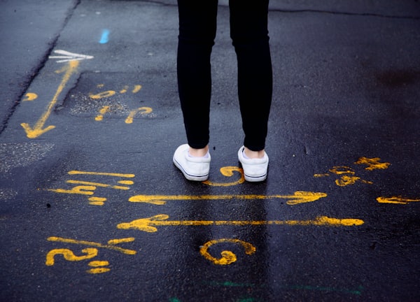 person in black pants and white sneakers standing on black asphalt road