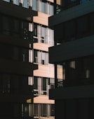 A modern architectural façade with a series of rectangular windows, capturing the play of light and shadow across the building surfaces. The design features alternating sections of light and dark materials, creating a geometric pattern.