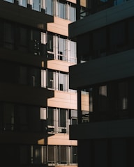 A modern architectural façade with a series of rectangular windows, capturing the play of light and shadow across the building surfaces. The design features alternating sections of light and dark materials, creating a geometric pattern.
