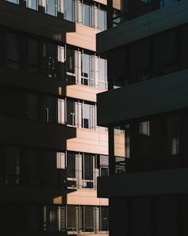 A modern architectural façade with a series of rectangular windows, capturing the play of light and shadow across the building surfaces. The design features alternating sections of light and dark materials, creating a geometric pattern.