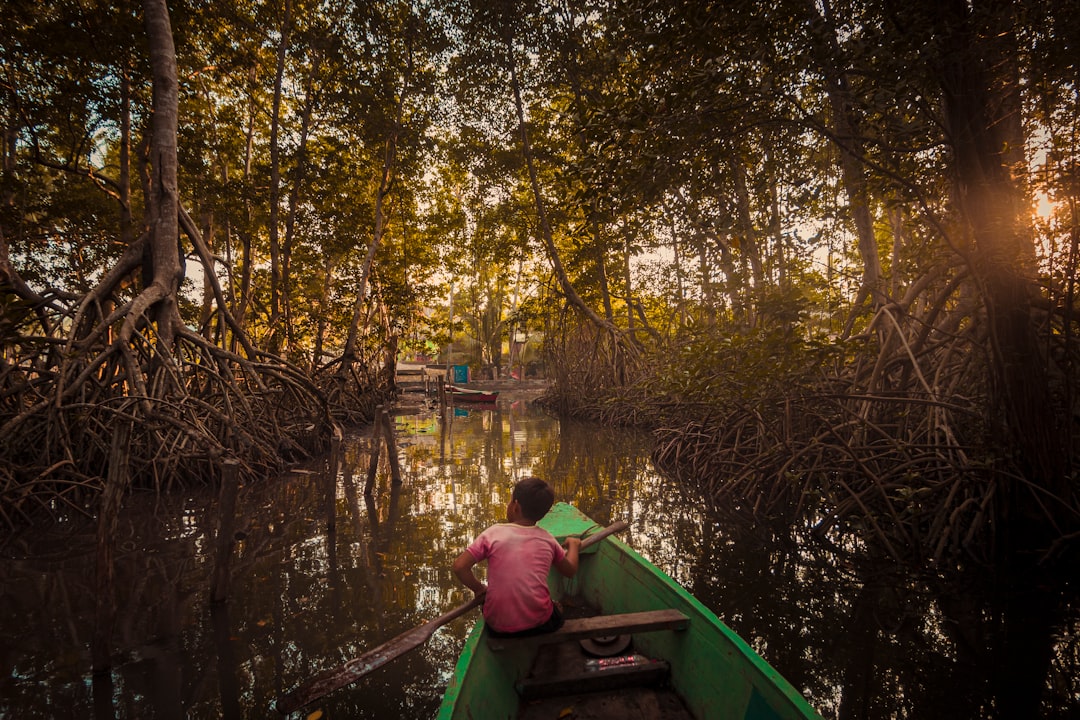 man in red shirt sitting on green boat on river during daytime