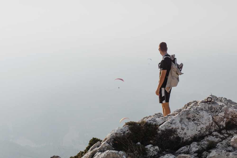 Mann in schwarzer Jacke und braunen Shorts steht tagsüber auf Felsen