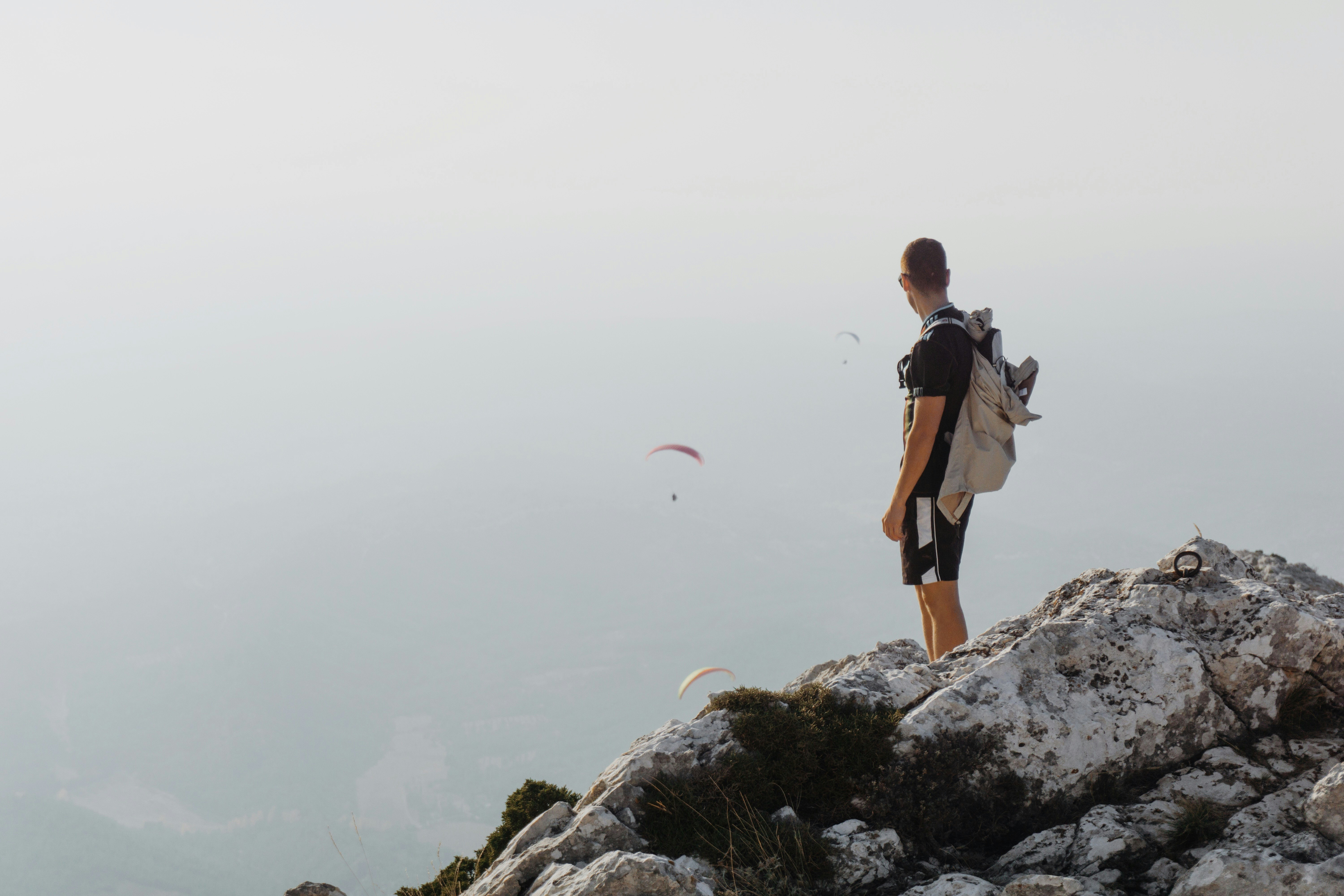 A man at the top of mountain watching three paragliders