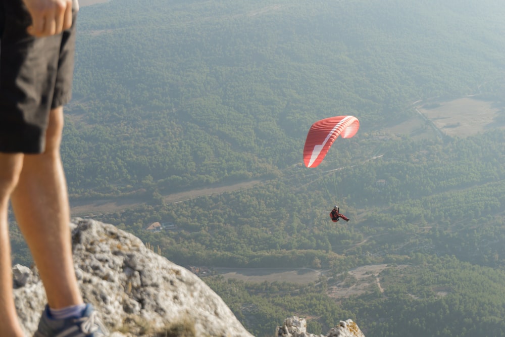 person in black jacket riding red parachute over green mountains during daytime