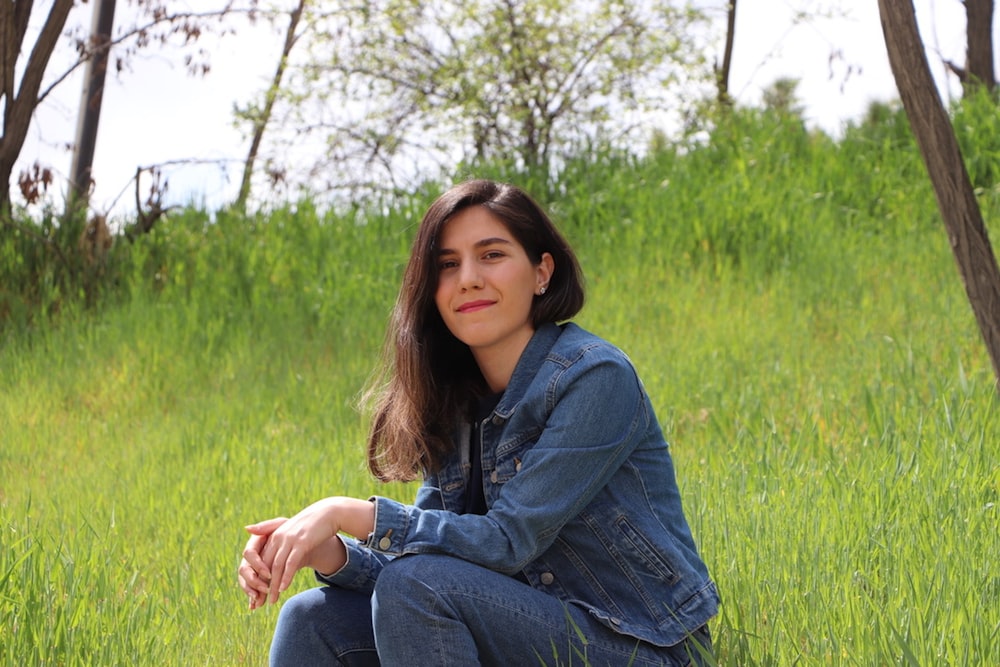 woman in blue denim jacket and blue denim jeans sitting on green grass field during daytime