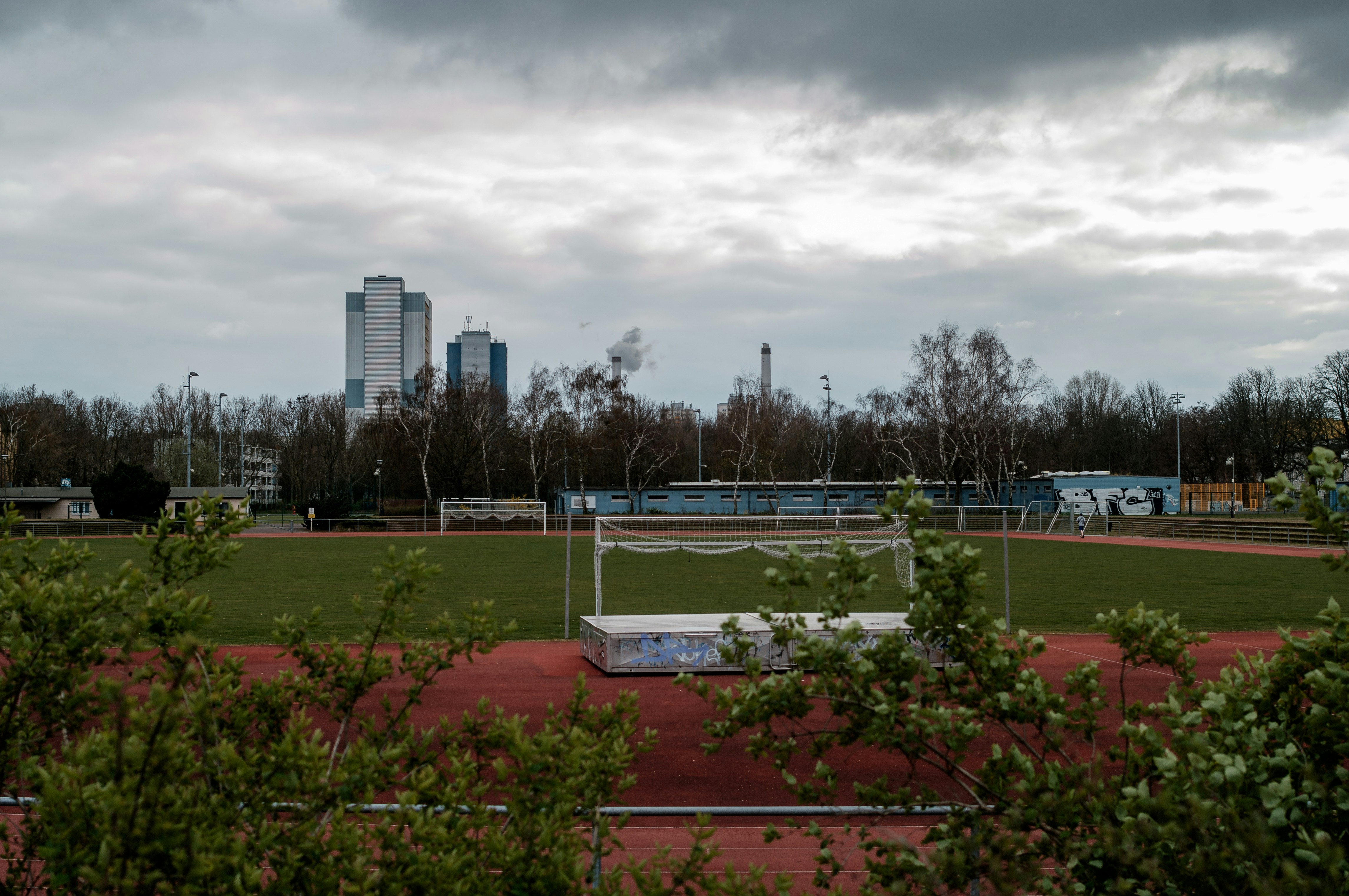 green grass field near city buildings under white clouds during daytime