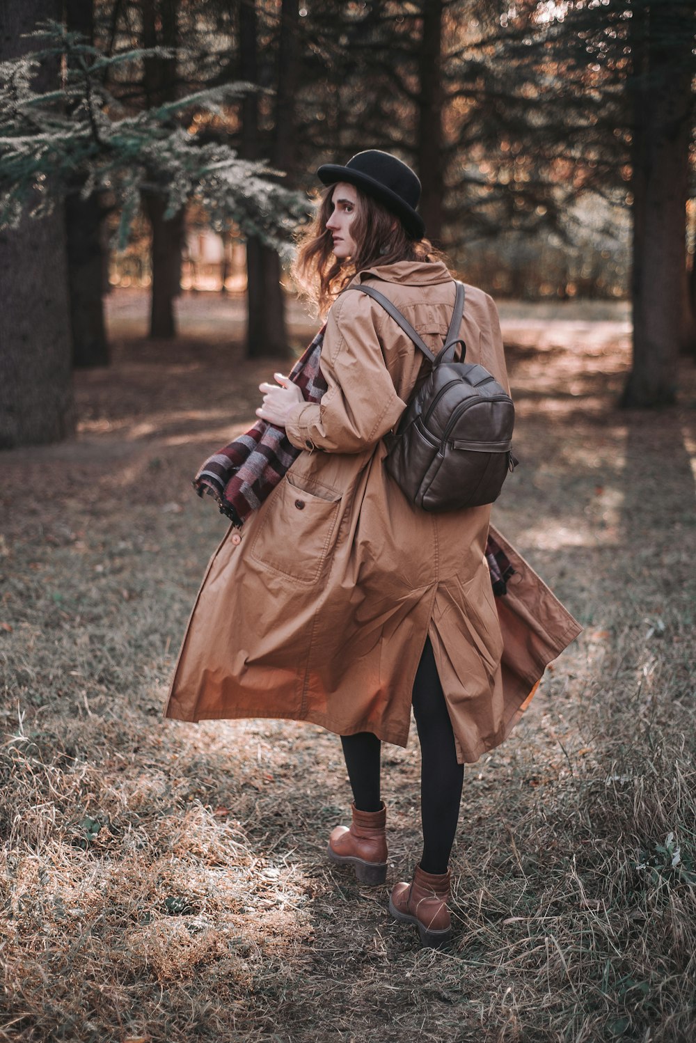 woman in brown coat and black boots walking on green grass field during daytime