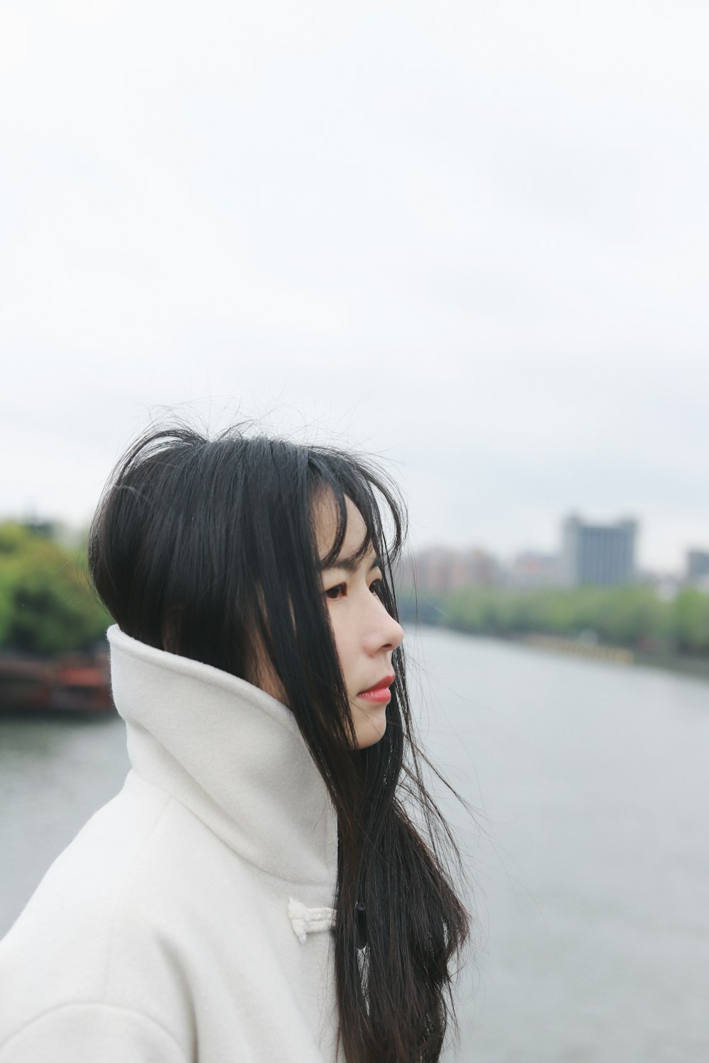 woman in white coat standing near body of water during daytime