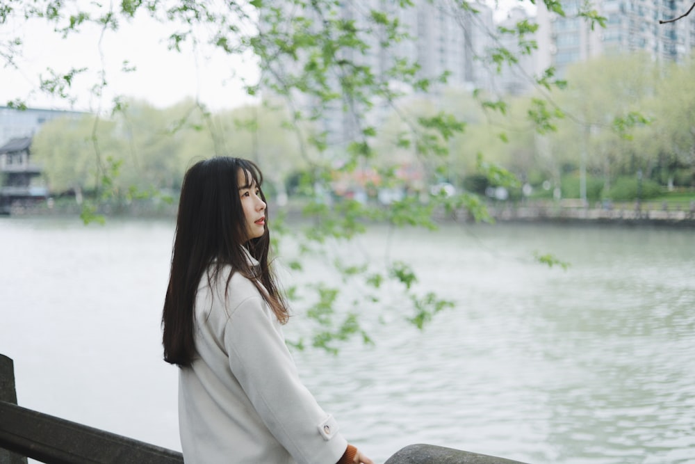 woman in white long sleeve shirt sitting on gray concrete bench near body of water during