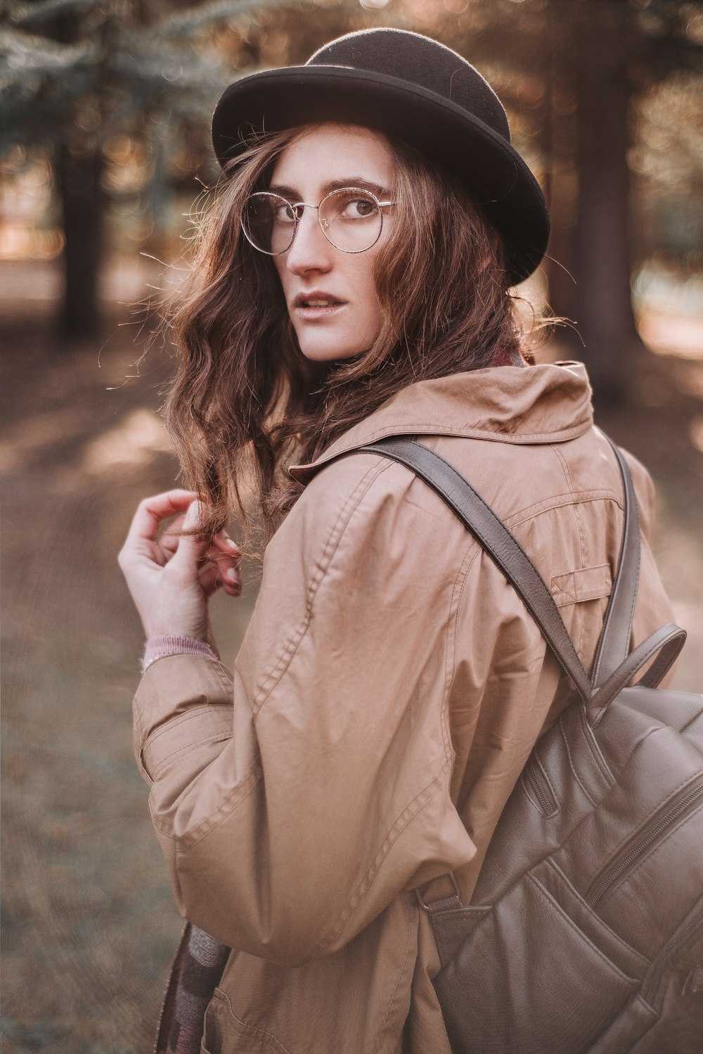 woman in brown leather jacket wearing black hat and black framed eyeglasses