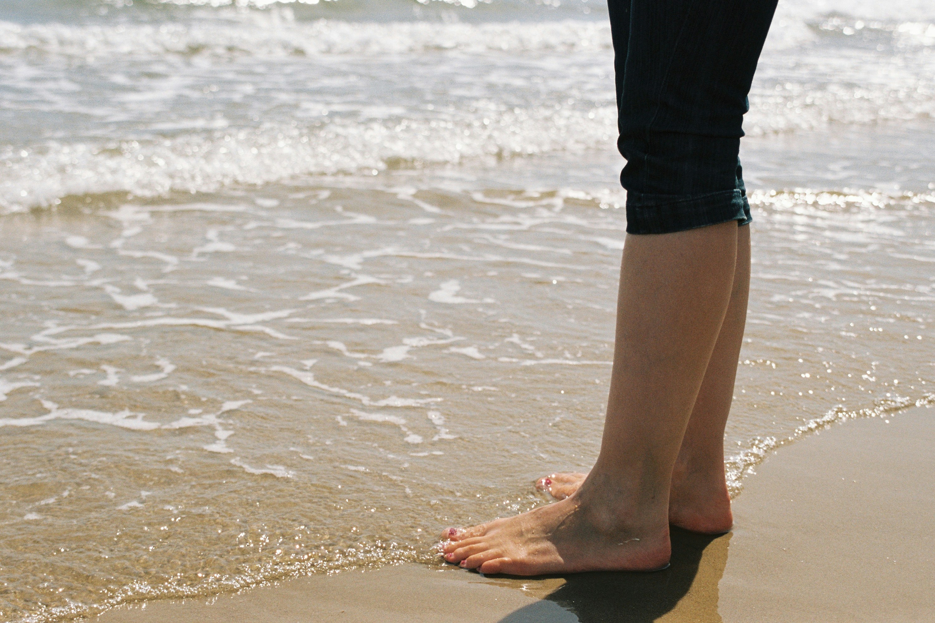 A woman wearing cut off jeans with bare feet in the sea. Shot on film.