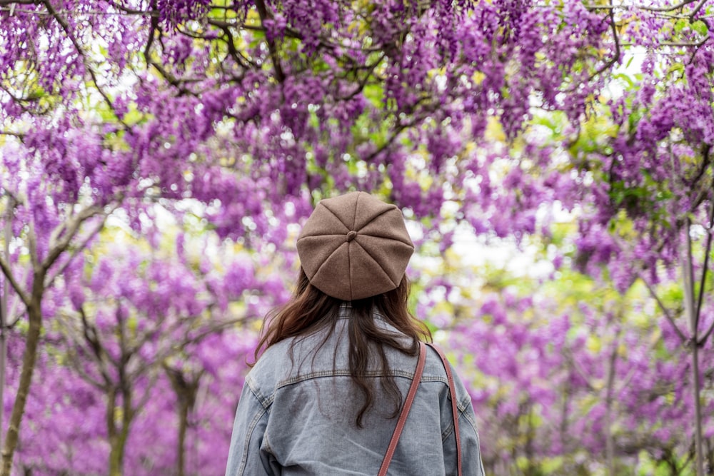 Mujer con sudadera con capucha gris de pie cerca de flores púrpuras durante el día