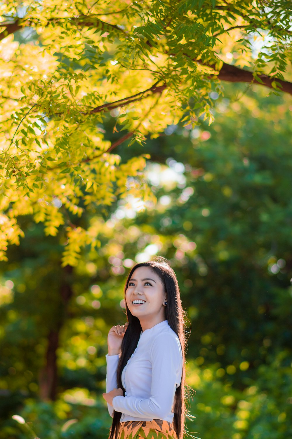 Mujer con camisa blanca de pie bajo un árbol verde durante el día