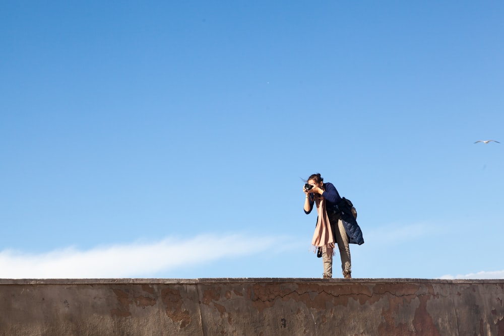 man in black jacket and black pants standing on gray concrete wall under blue sky during