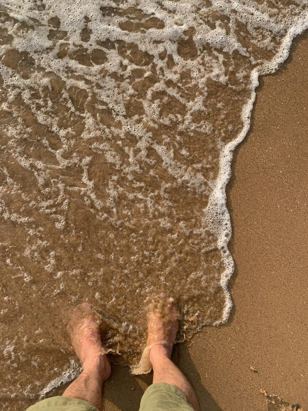 Persona in piedi sulla spiaggia di sabbia marrone durante il giorno