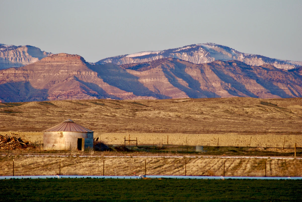 A round metal shed on farmland near Fruita, with snow-streaked cliffs behind