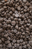 A large pile of chocolate chips tightly packed together, displaying a natural variation in color and texture with some chips exhibiting a slight sheen.