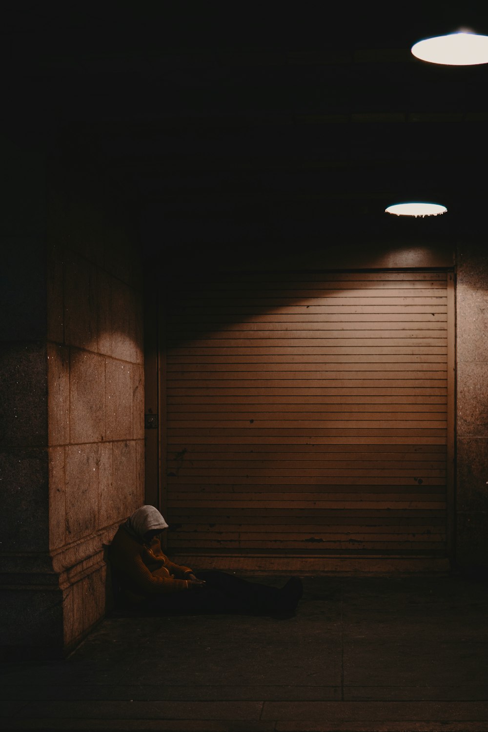 man in black jacket and blue denim jeans sitting on floor