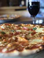 Close-up of a wood-fired pizza with bubbling cheese and fresh basil on top.