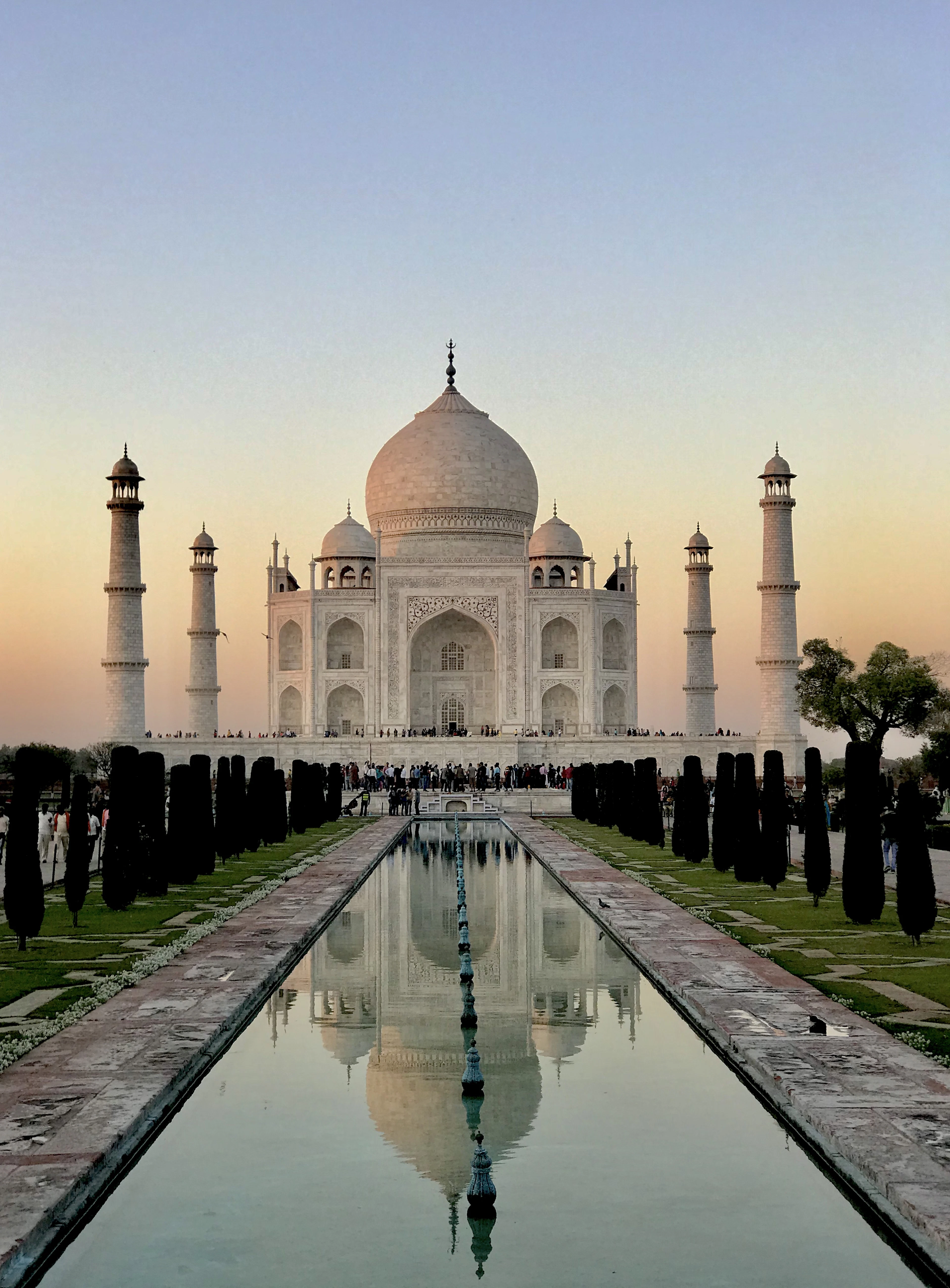 The Taj Mahal at dawn down the length of its reflecting pool, dark cypresses lining both banks
