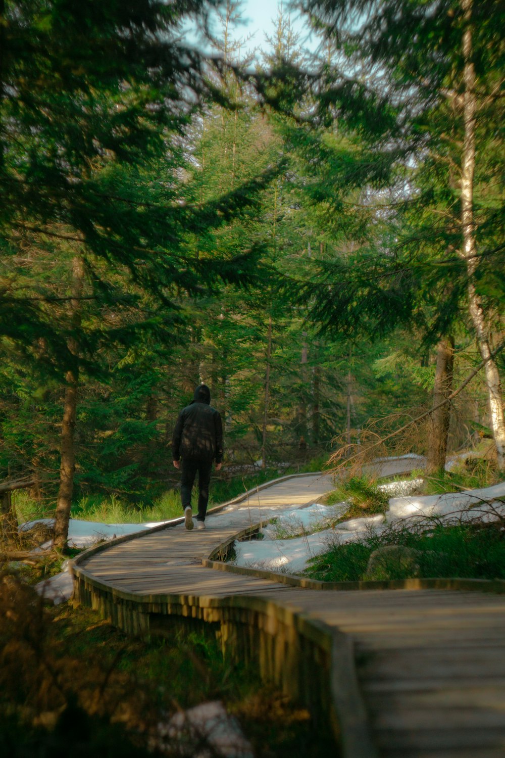 man in black jacket walking on wooden bridge