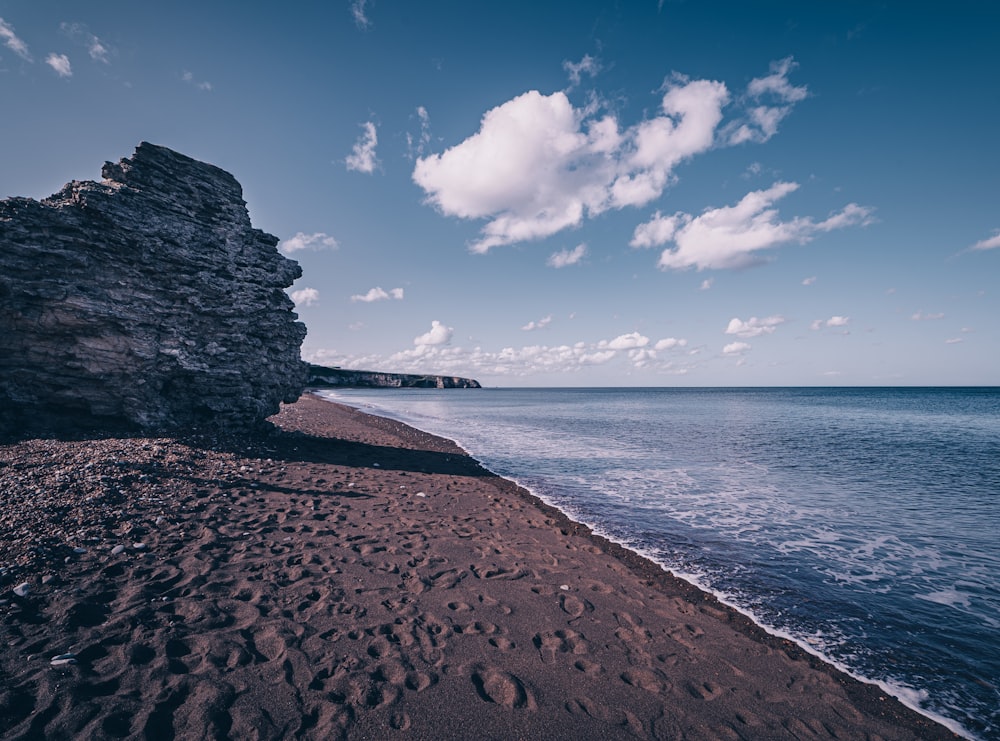 brown sand beach near body of water under blue sky during daytime