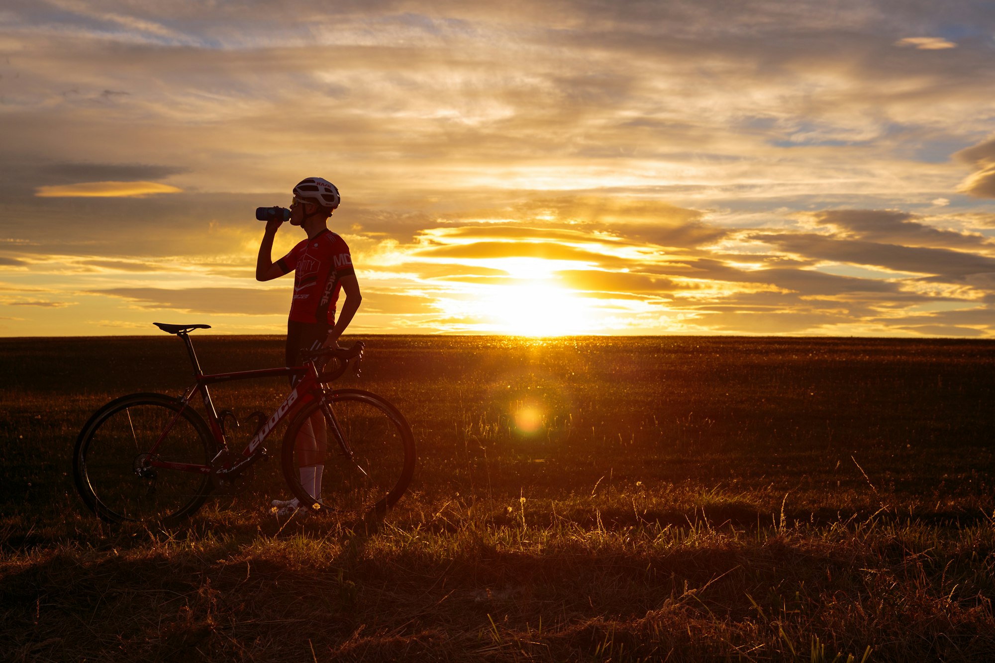 A cyclist taking a drink at sunset.