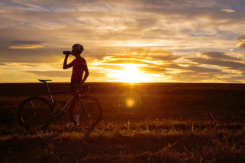 man riding bicycle on green grass field during sunset