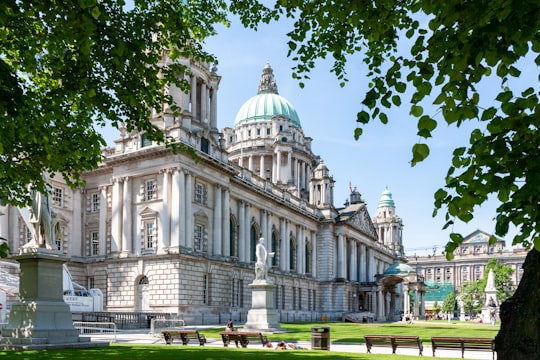 white concrete building near green trees under blue sky during daytime in Belfast City Hall United Kingdom
