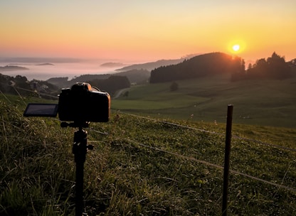 A sleek film camera on a tripod capturing a golden hour outdoor scene.