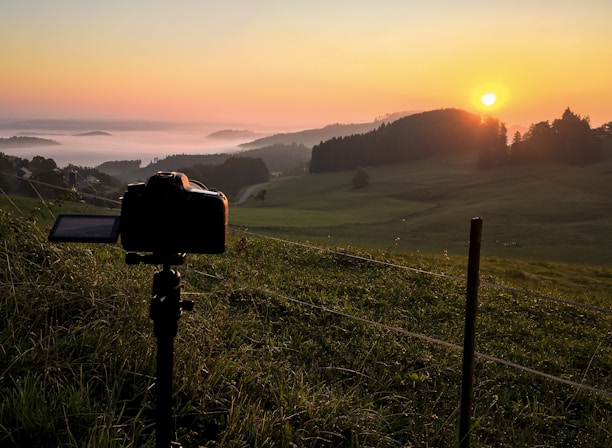 A filmmaker setting up a camera in a scenic Cantal landscape during golden hour.