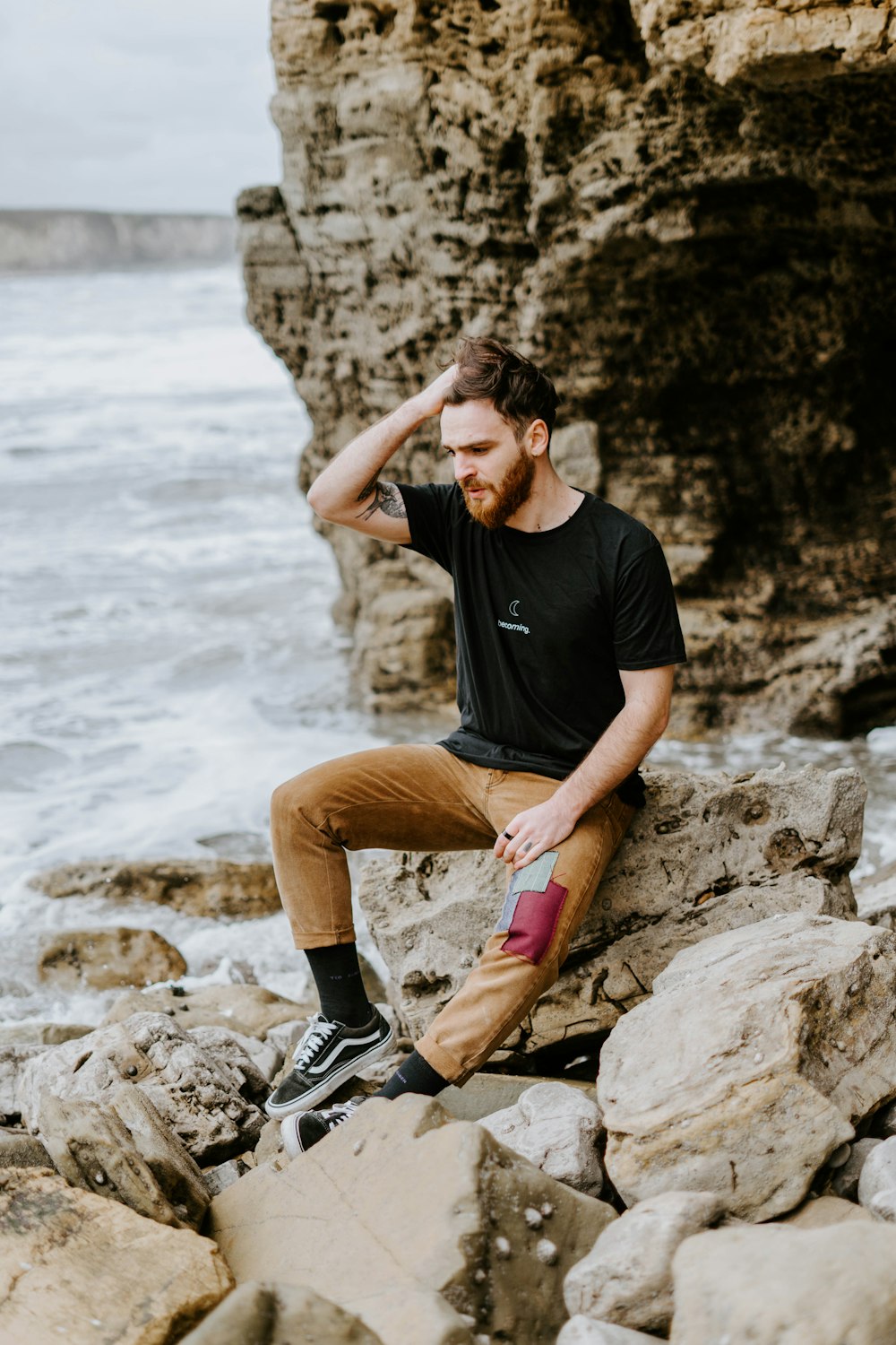 man in black t-shirt and brown shorts sitting on rock near body of water during