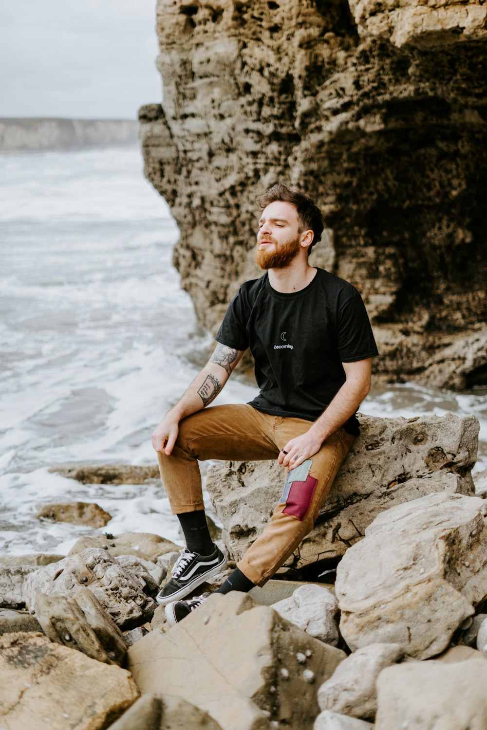 man in black crew neck t-shirt and brown shorts sitting on rock near body of near on on on