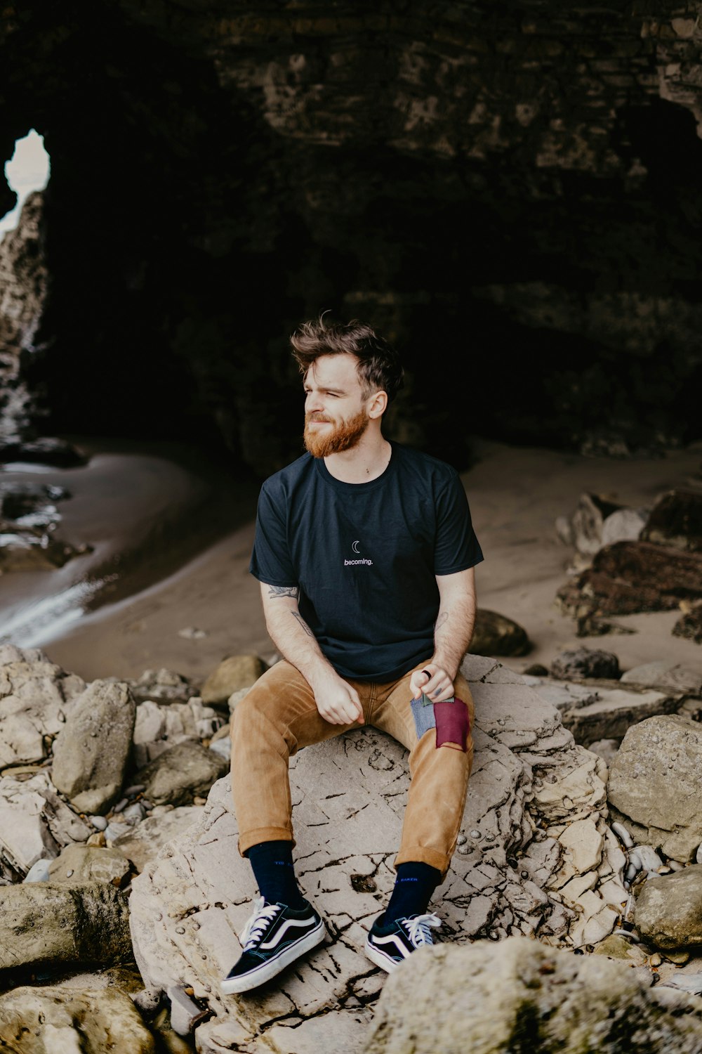man in black crew neck t-shirt and brown pants sitting on rock