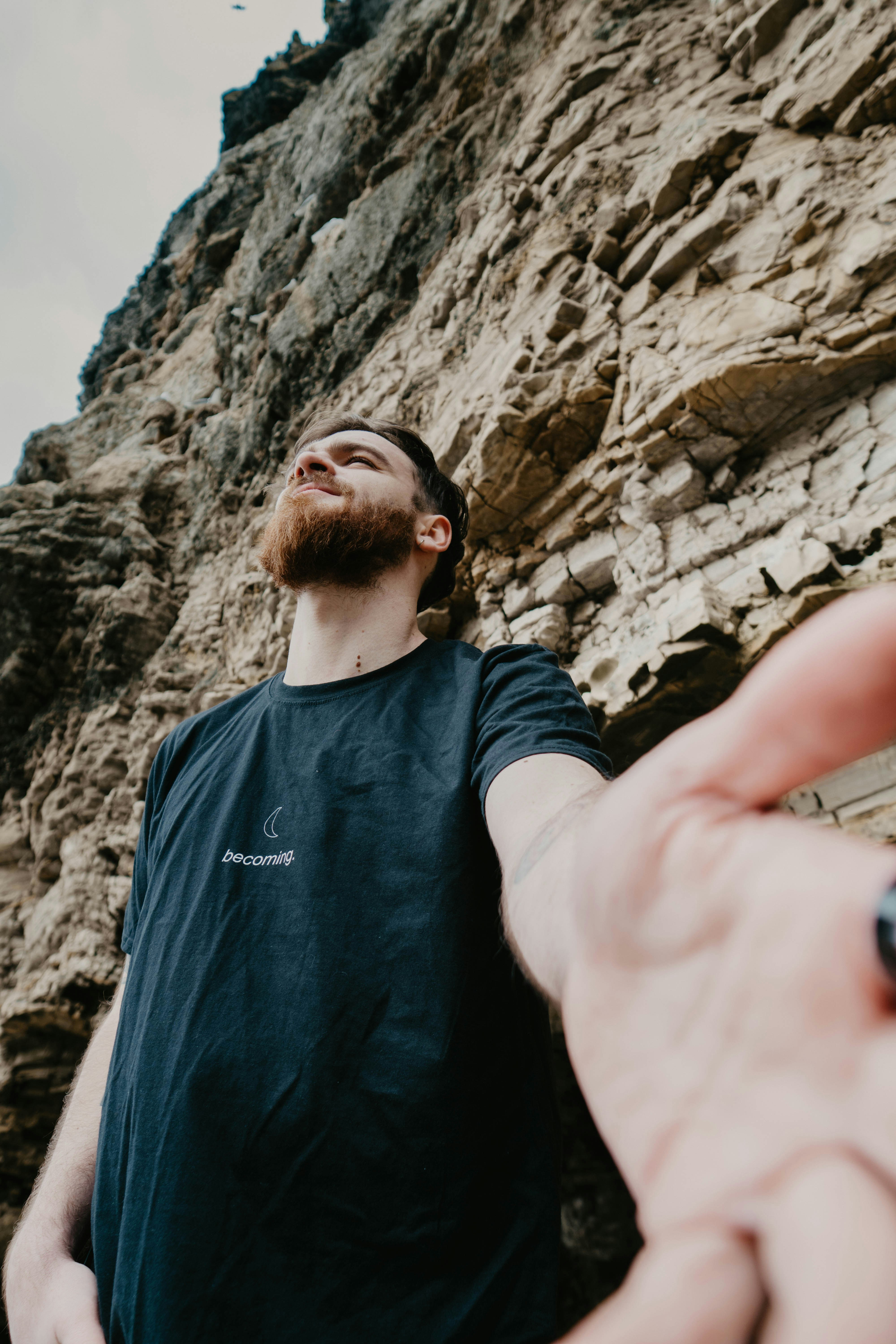 man in blue crew neck t-shirt standing near rock formation during daytime