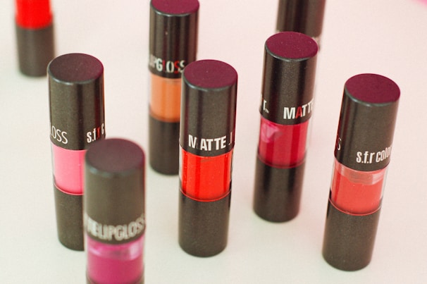 A collection of lipsticks in black containers with various shades of red, pink, and orange, displayed upright on a light surface.