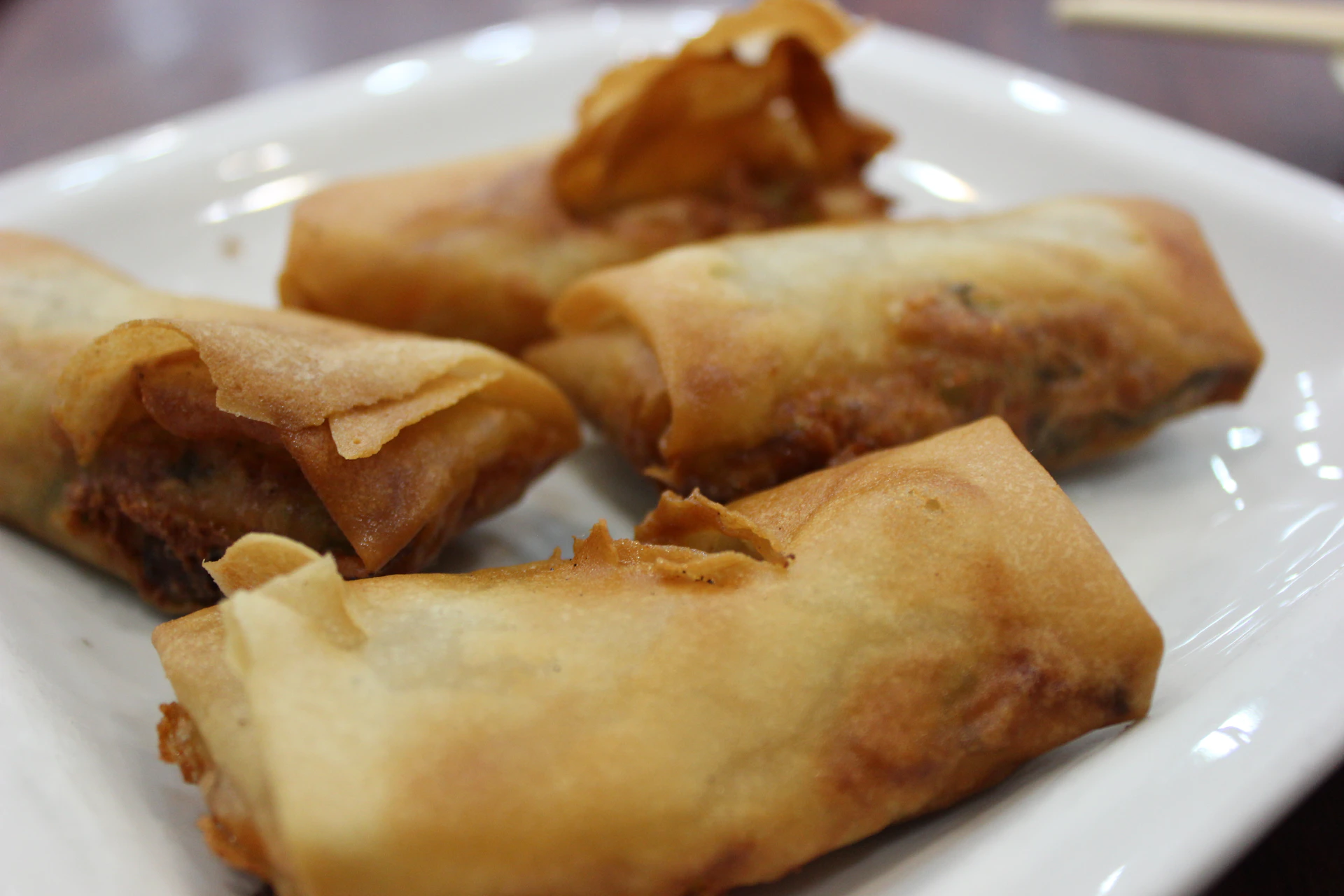 A close-up of golden-brown crispy spring rolls served with a tangy dipping sauce, artfully arranged on a rustic wooden platter.