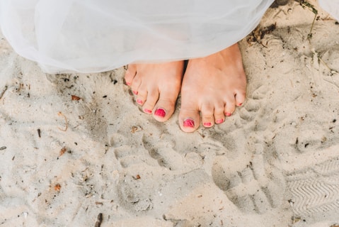 person with red pedicure standing on white textile